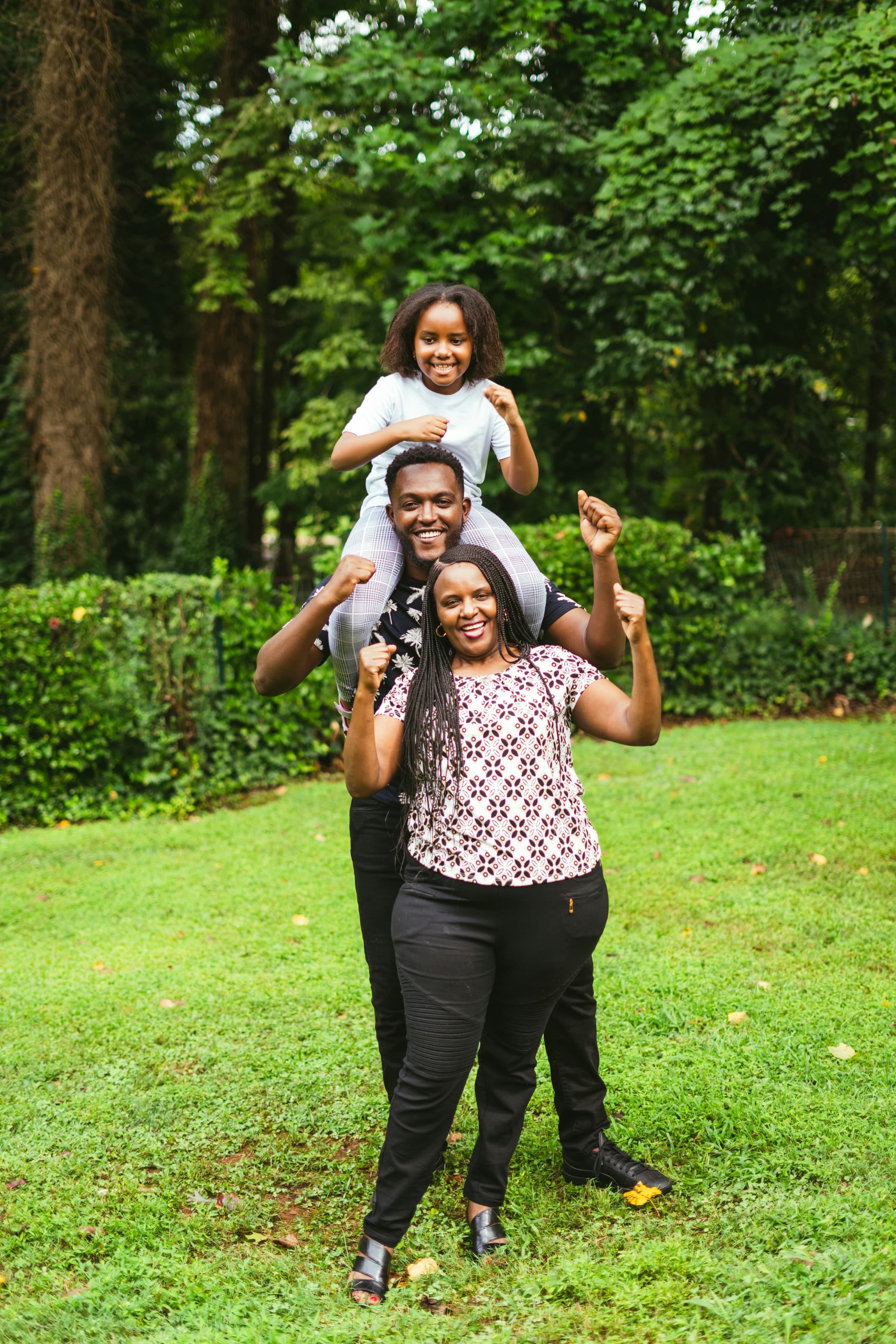 A joyful family celebrating - a young girl on her father's shoulders with arms raised, mother standing beside them with fists raised in triumph